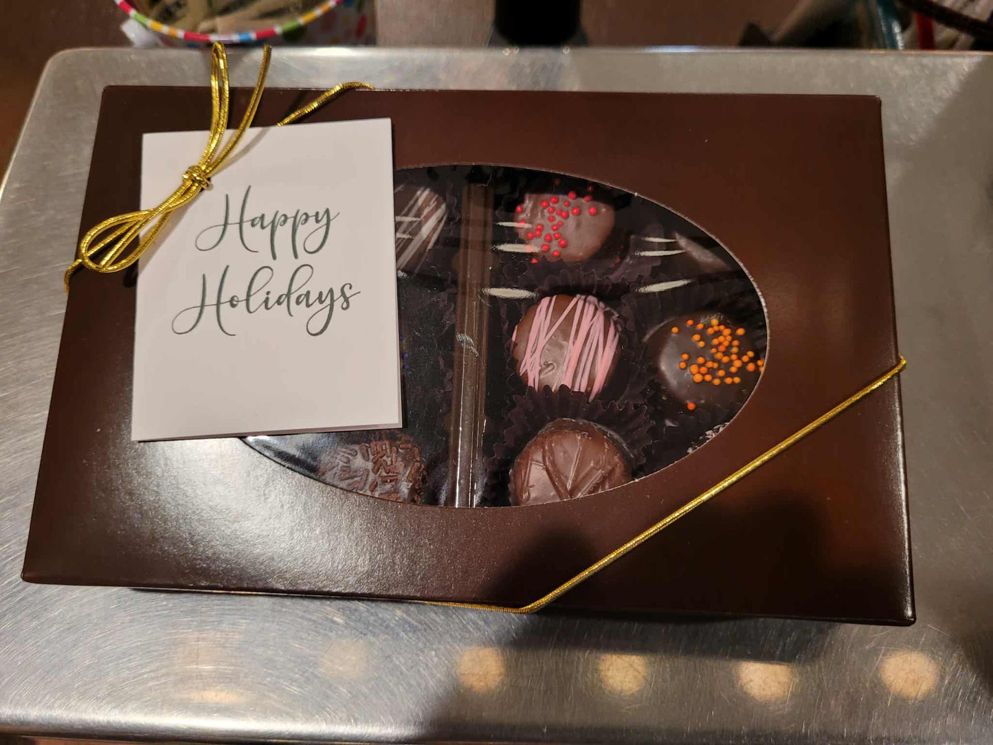 Box of chocolates with a 'Happy Holidays' tag on a reflective surface